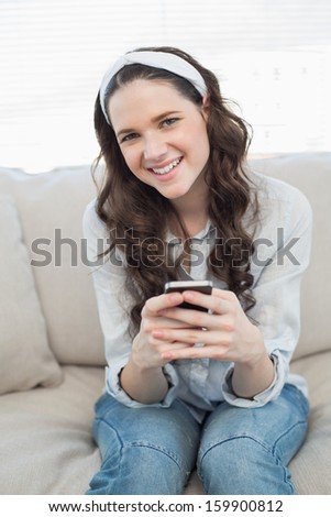 Pretty casual woman text messaging on her smartphone while sitting on a cosy couch