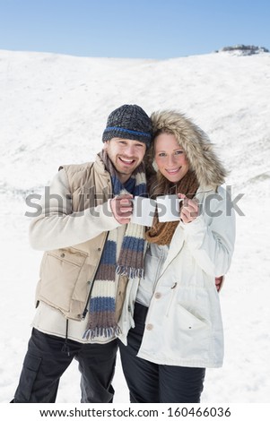 Portrait of a cheerful young couple in warm clothing with coffee cups on snow covered landscape