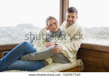 Portrait of a young couple in winter clothing sitting against cabin window