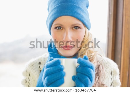 Close-up portrait of a cute woman with coffee cup in warm clothing against cabin window