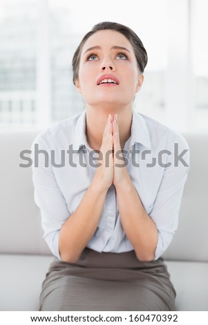 Worried well dressed woman sitting with joined hands as she looks up at home