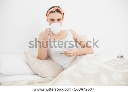 Pretty woman drinking a cup of tea lying in her bed in her bedroom