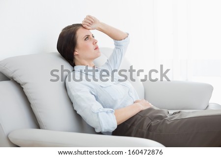 Serious well dressed young woman sitting on sofa at home