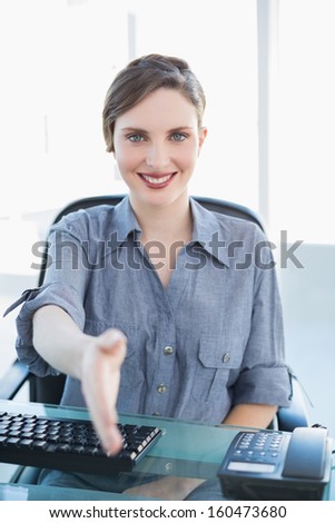 Friendly businesswoman welcoming while sitting at her desk smiling at camera