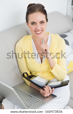 Portrait of a smiling young woman with personal organizer and laptop at home