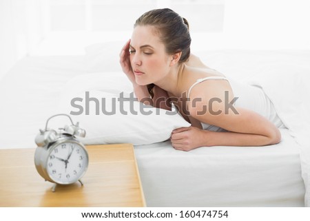Sleepy young woman in bed with alarm clock in foreground at bedroom