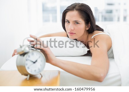 Portrait of a young woman in bed extending hand to alarm clock at home