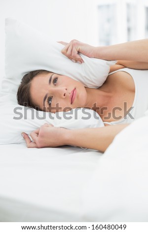 Close-up of a young woman covering ears with pillow in bed