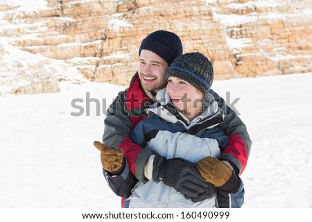 Happy man embracing woman from behind on snow covered landscape