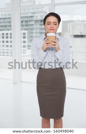 Young elegant businesswoman enjoying coffee smell with eyes closed in bright office