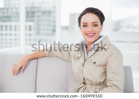 Portrait of a smiling well dressed young woman sitting on sofa at bright home