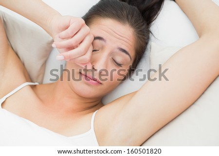 Close-up of a beautiful young woman rubbing eye in bed
