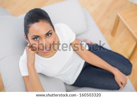 Lovely casual woman smiling at camera sitting on couch in bright living room