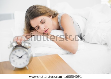 Cute peaceful woman lying on her bed sleeping turning off the alarm clock