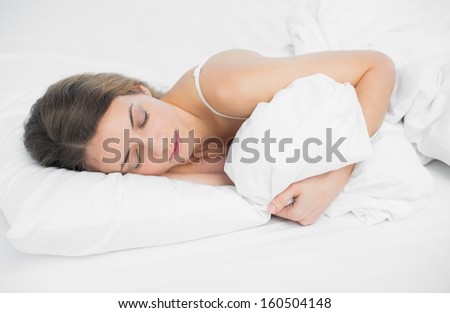 Sweet brunette woman sleeping holding her cover in bright bedroom