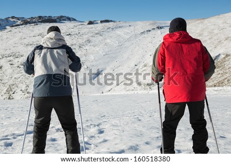 Rear view of a couple with ski poles on snow covered landscape against clear blue sky