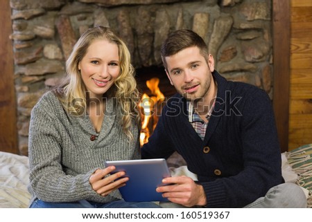 Portrait of a lovely young couple using tablet PC in front of lit fireplace