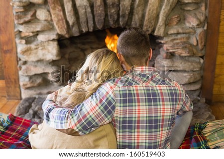 Rear view of a romantic young couple sitting in front of lit fireplace