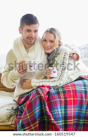 Portrait of a loving young couple in winter clothing with coffee cups against cabin window