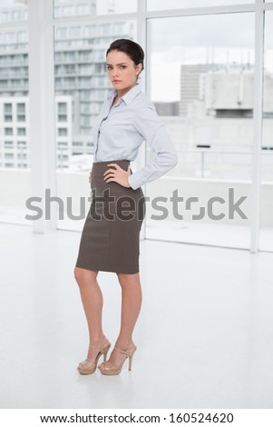 Full length portrait of an elegant businesswoman standing with hands on hips in office