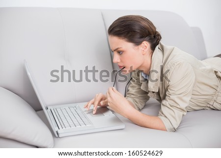 Side view of a beautiful young woman using laptop on sofa at home
