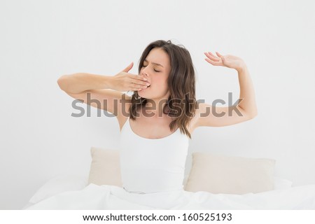 Young woman yawning as she stretches in bed at home