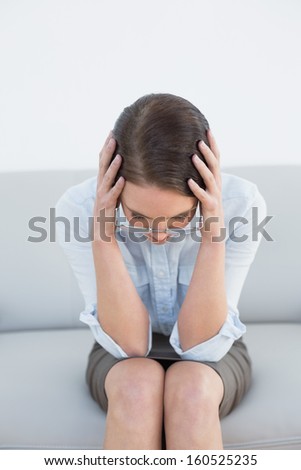 Worried well dressed young woman sitting with head in hands on sofa at home