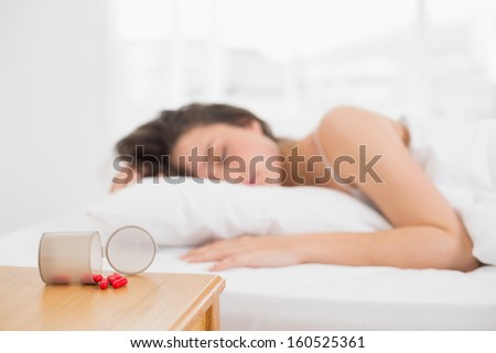 Young Woman Sleeping In Bed By Bottle Of Pills On Table At Home