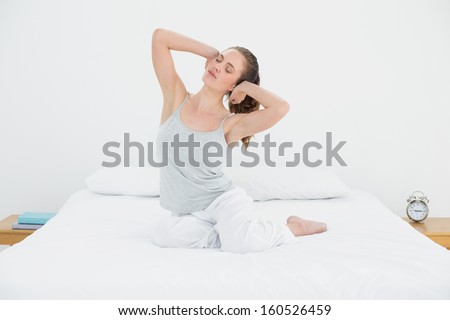 Sleepy young woman waking up in bed and stretching her arms