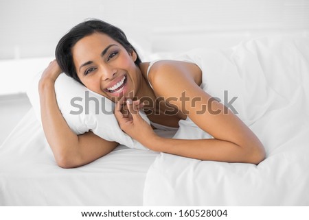 Content laughing woman lying under the cover on her bed looking at camera