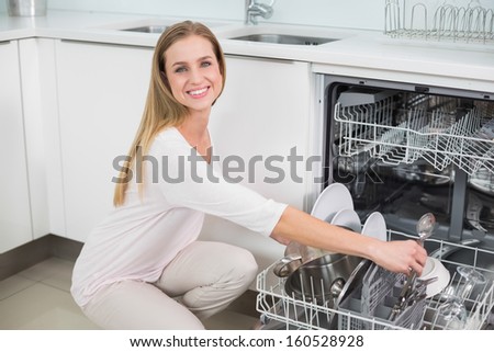 Cheerful gorgeous model kneeling next to dish washer in bright kitchen