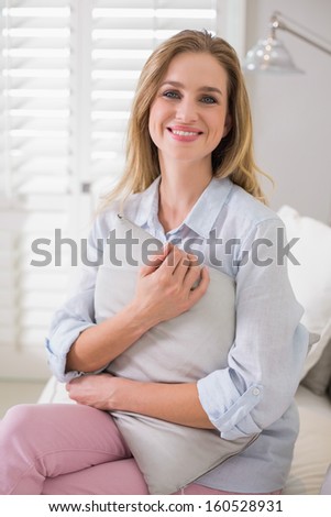 Casual cheerful blonde sitting on couch holding pillow in bright living room