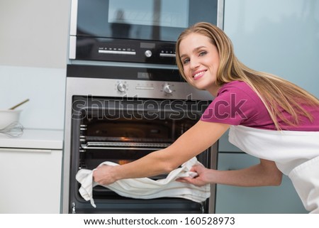 Casual happy woman taking baking tray out of oven in bright kitchen