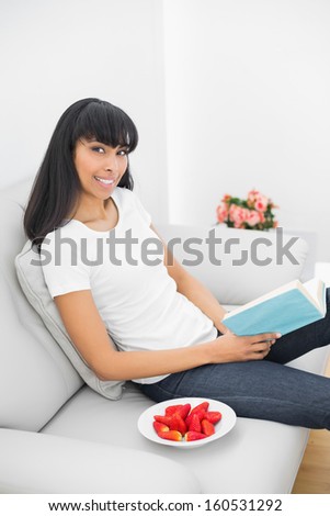 Beautiful relaxing woman holding a book sitting on a couch in bright living room