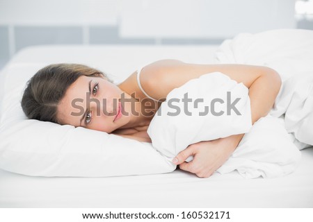 Attractive calm woman lying on her bed holding her cover looking at camera
