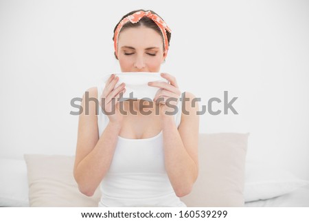Young woman smelling on a handkerchief sitting on her bed in her bedroom