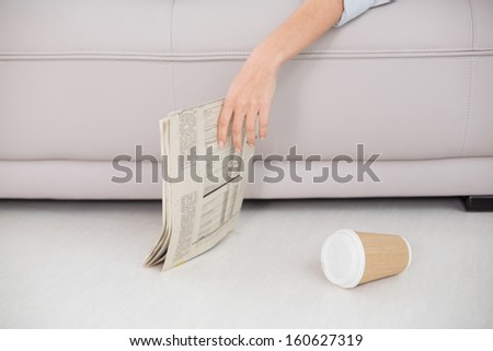 Mid section of an asleep woman holding newspaper on sofa at home