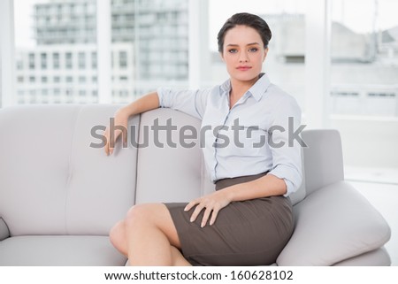 Portrait of a serious well dressed young woman sitting on sofa at bright home
