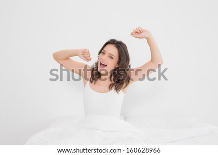 Portrait of a smiling young woman waking up in bed and stretching her arms
