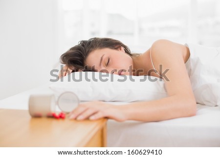 Young woman sleeping in bed by bottle of pills on table at home