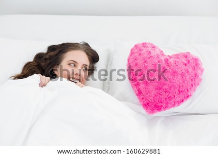 Beautiful young woman lying in bed with heart  shaped pillow cover