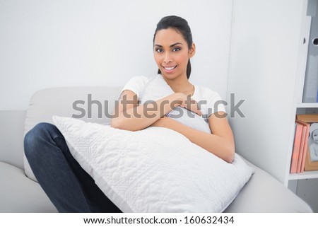 Sweet casual woman holding a pillow while lying on couch smiling at camera