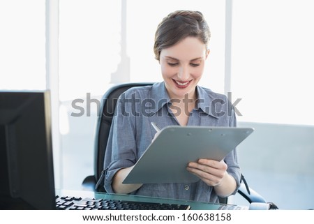 Content attractive businesswoman writing on clipboard sitting at her desk in the office