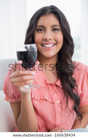 Pleased cute brunette sitting on couch holding wine glass in bright living room
