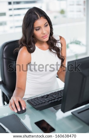 Calm cute businesswoman sitting behind desk at computer in bright office