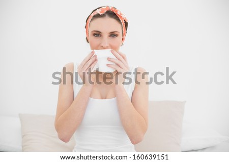 Woman smelling on a handkerchief looking into the camera sitting on her bed