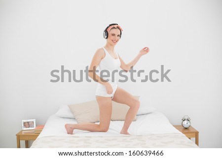 Pretty woman playing air guitar on her bed while listening to music