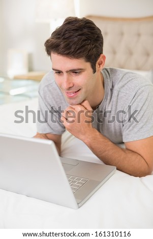 Casual smiling young man using laptop in bed at home