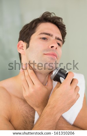 Close up of a handsome young shirtless man shaving with electric razor