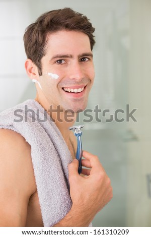 Side view portrait of a smiling handsome young man shaving in the bathroom